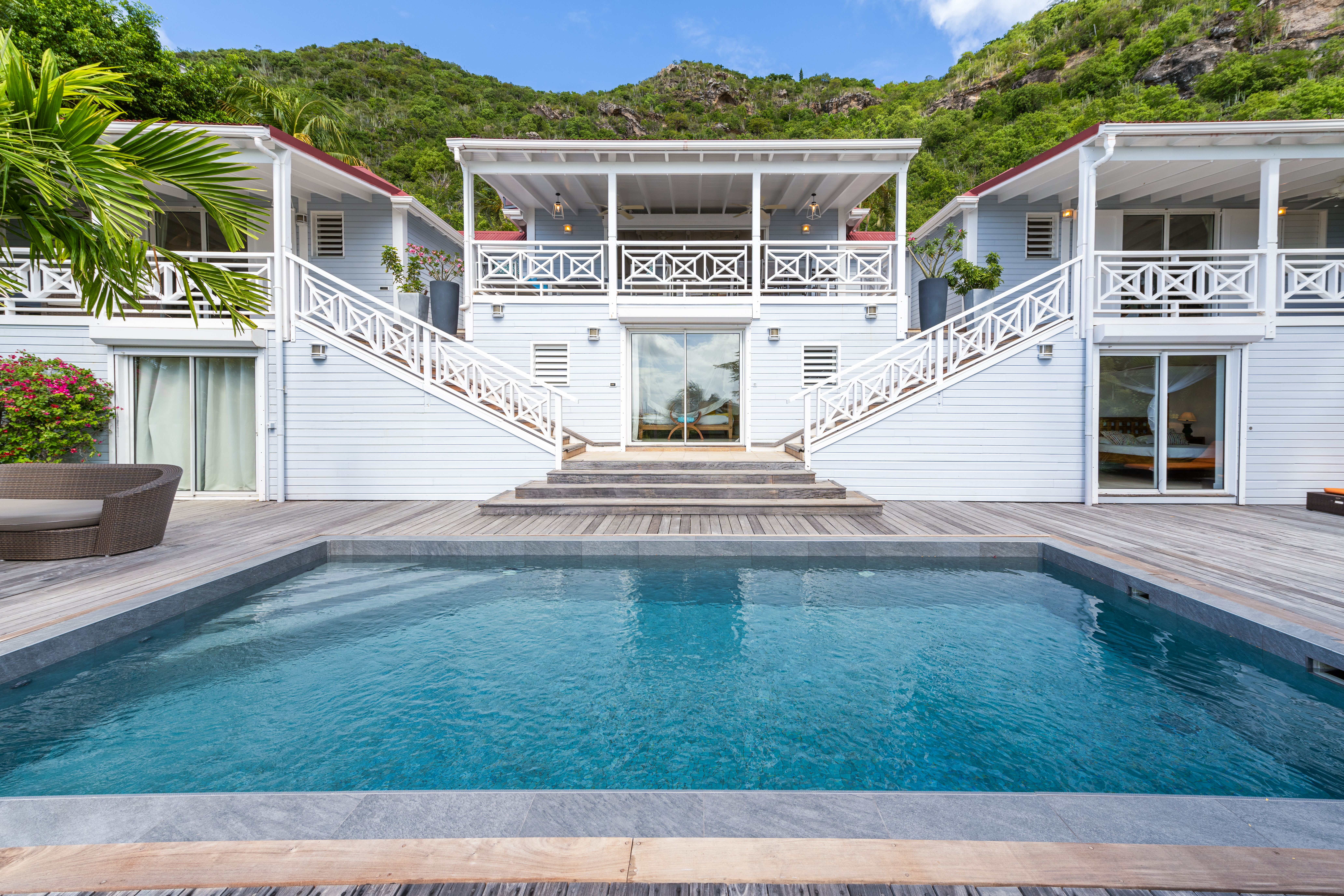 Swimming pool with deck facing white colonial-style villa surrounded by green hills in St Barts villa rental