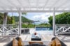Covered terrace with cushioned lounge chairs overlooking a private pool and panoramic views of Corossol Bay in St Barts, ideal for luxury Caribbean villa rentals