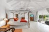 Spacious Caribbean villa bedroom in Corossol, St Barts, featuring a four-poster bed with orange accents, vaulted white ceiling, and terrace access with ocean views