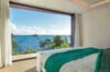 Luxury villa bedroom in St Barts with panoramic ocean view, floor-to-ceiling window, and elegant minimalist decor with green accents