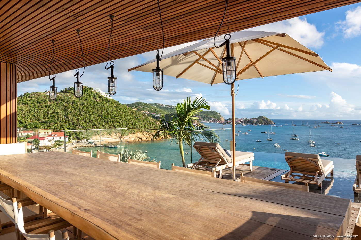 Luxury St Barts villa terrace with long wooden dining table, pendant lights, sun loungers, and panoramic ocean views