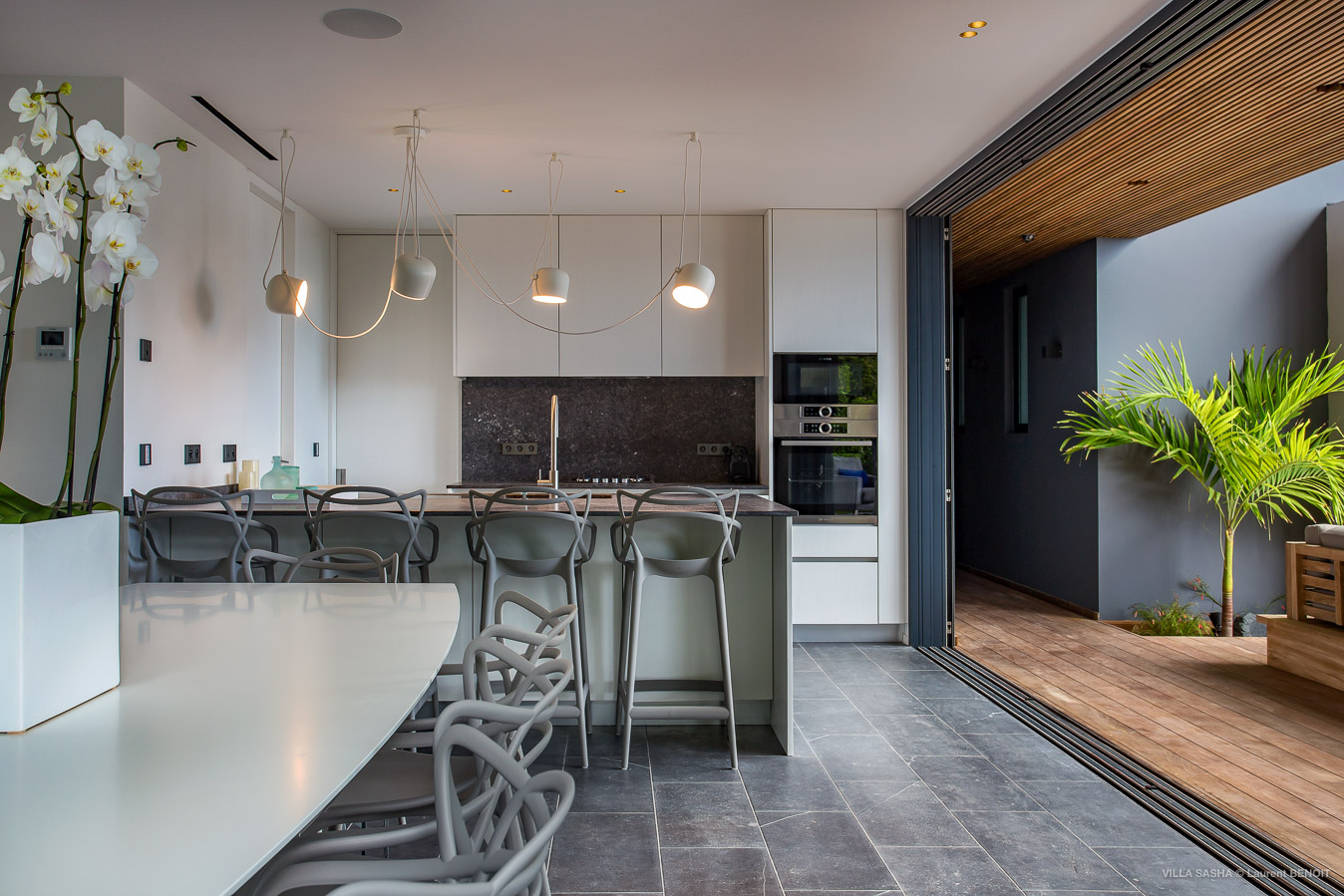 Contemporary villa kitchen with breakfast bar, designer chairs, and open-air access to terrace with tropical plants in St Barts rental