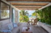 Sunny terrace in a St Barts villa with lounge seating, tropical plants, and ocean views beyond the garden