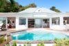 Sunlit pool in front of a modern white villa surrounded by lush greenery in St Barts