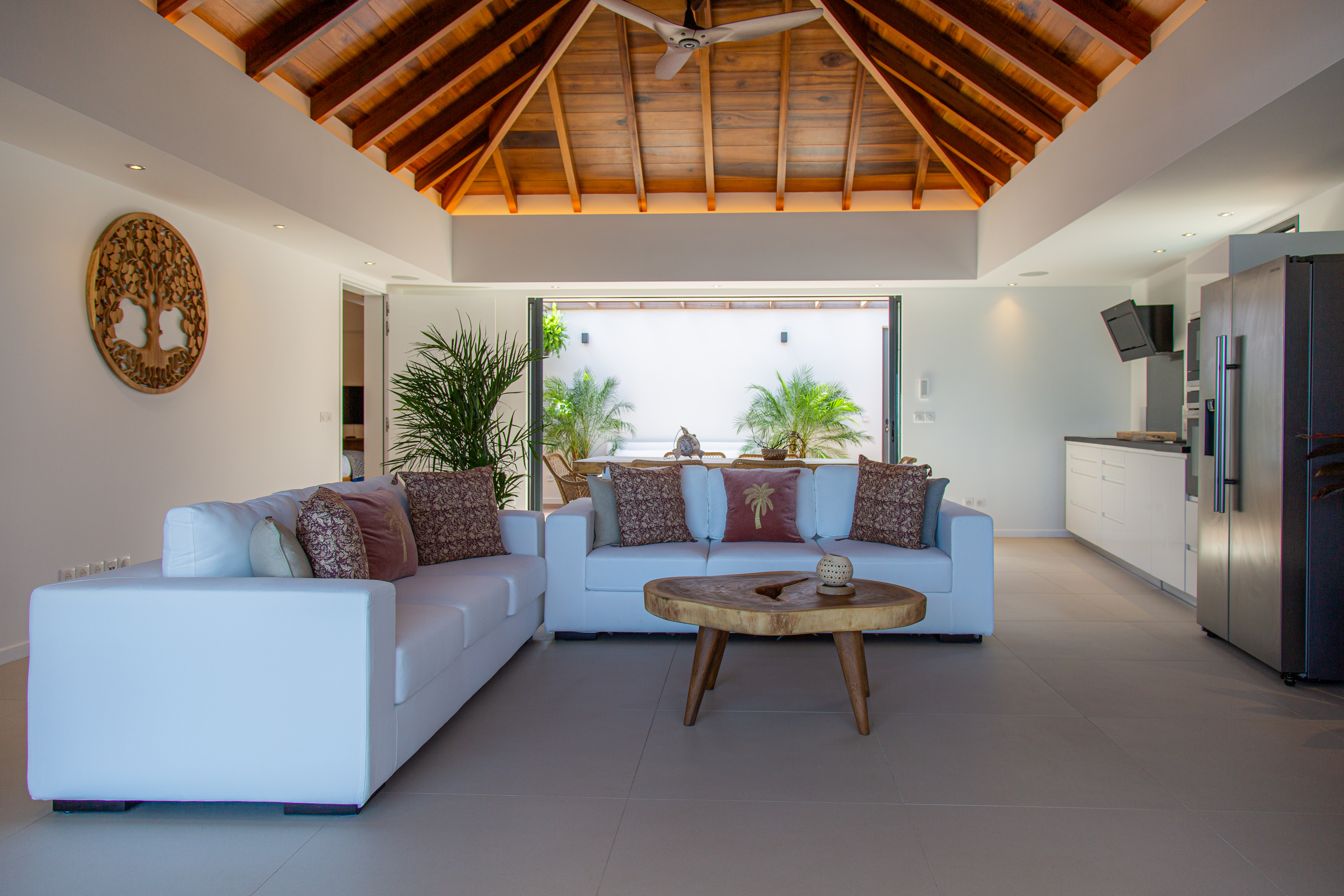 Bright living room with vaulted wooden ceiling, white sofas, and tropical garden view at a private villa rental in St Barts.