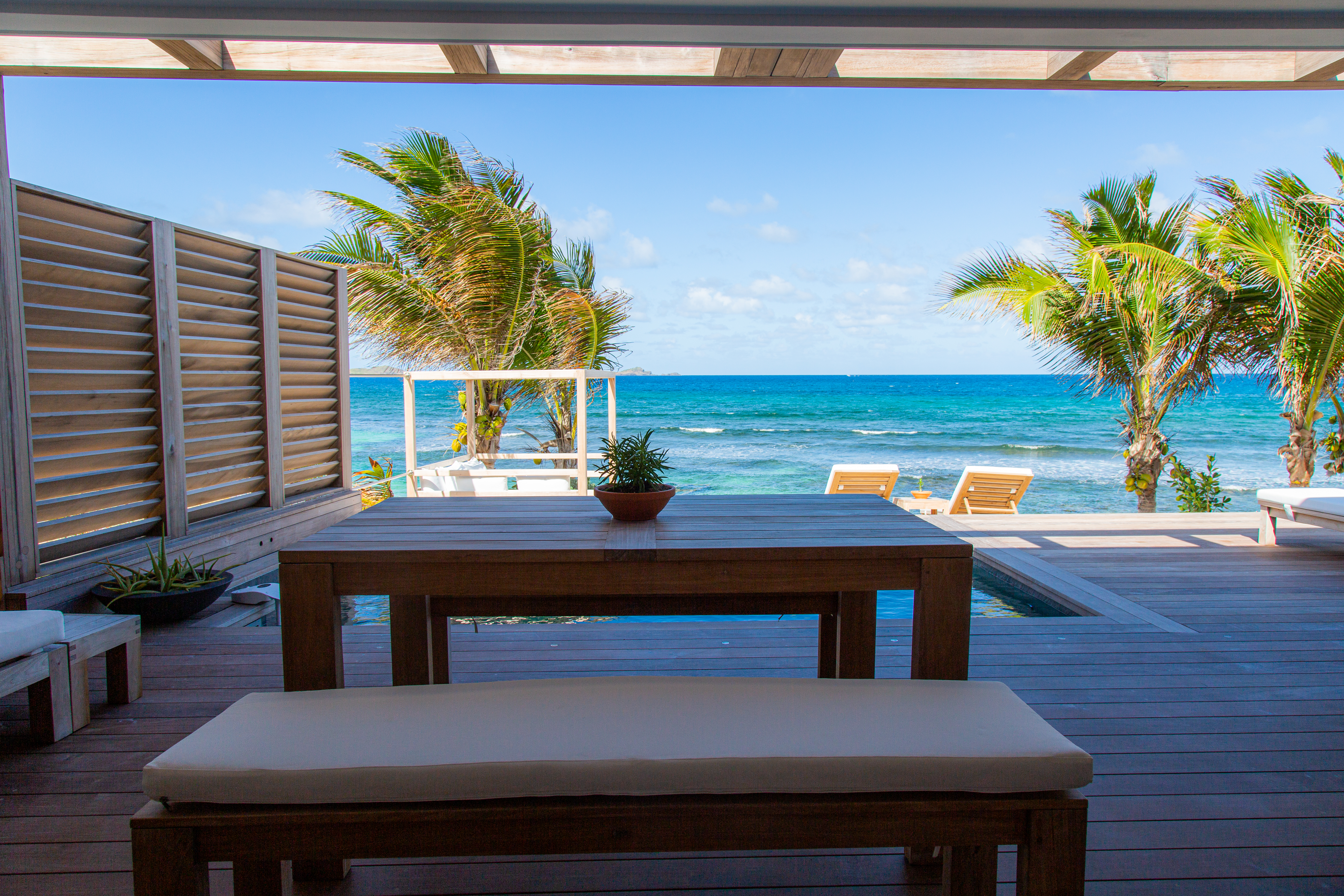 Covered terrace with wooden dining table and ocean view at beachfront luxury villa rental in St Barths