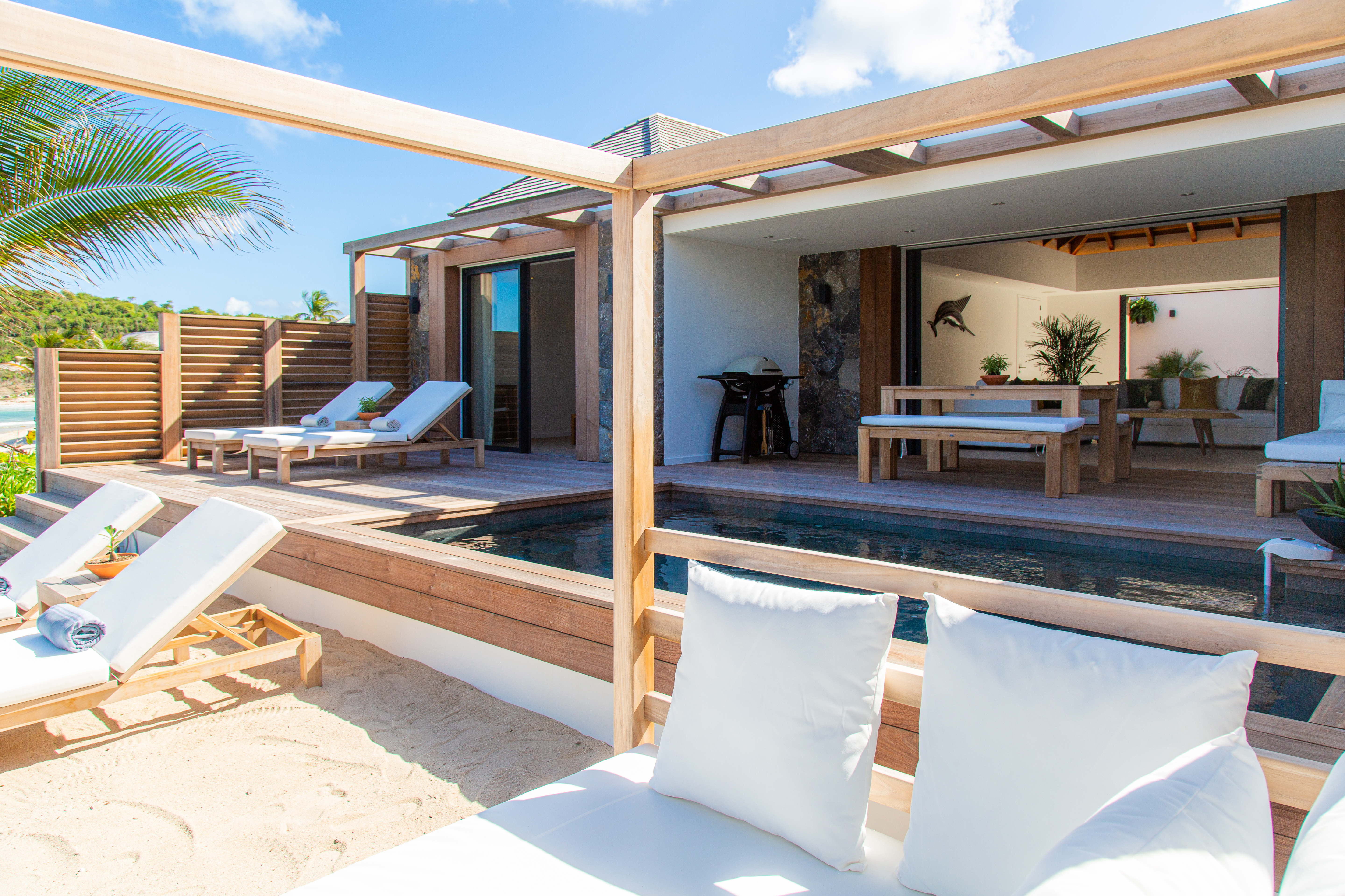 Beachfront villa in St Barts with sun loungers, shaded deck, and private plunge pool opening to an airy outdoor lounge