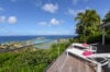Sunlit terrace of st barts villa with panoramic ocean view and palm-lined hillside.