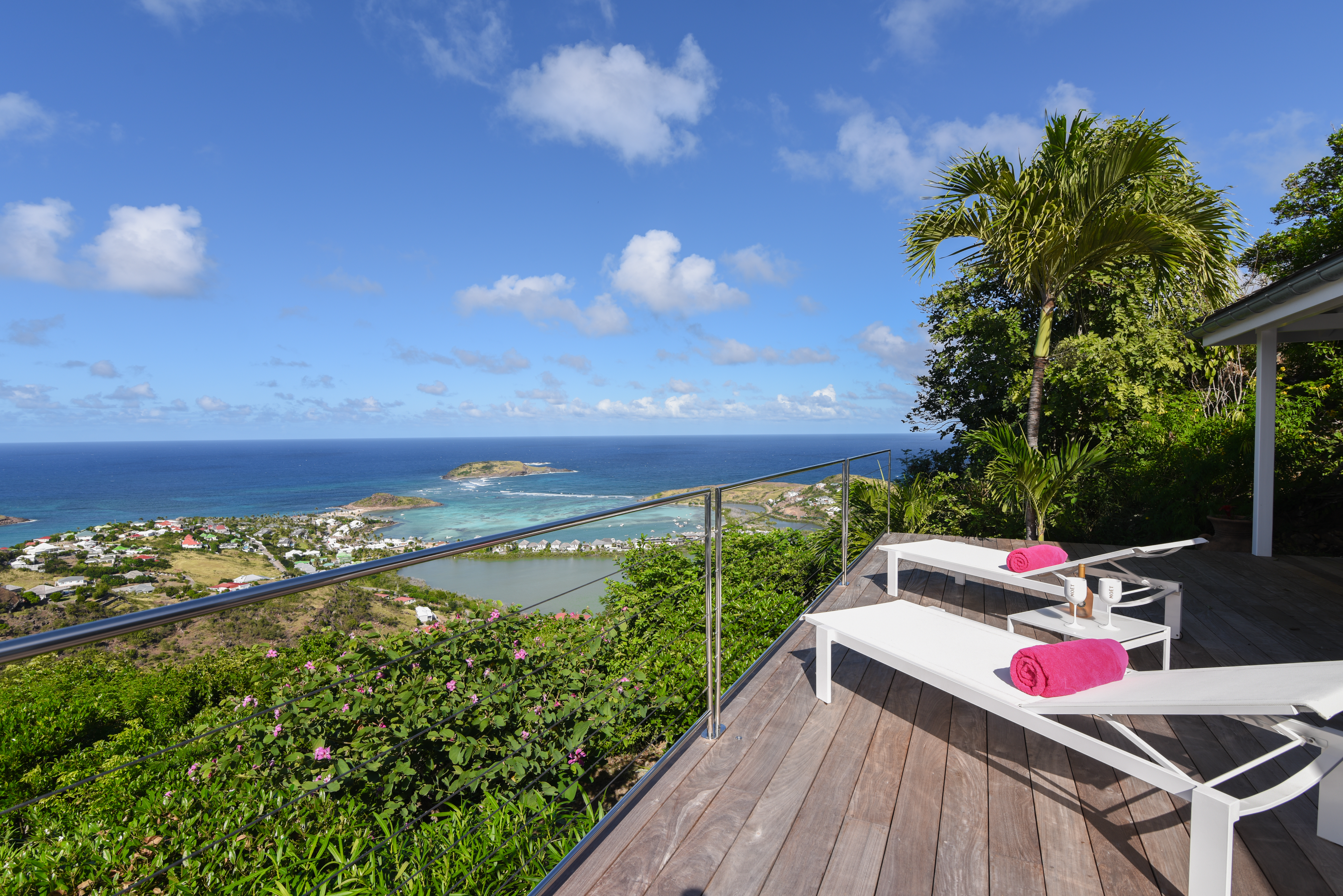 Sunlit terrace of st barts villa with panoramic ocean view and palm-lined hillside.