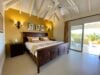 Elegant bedroom with carved wooden bed, vaulted ceiling, and terrace access at a luxury villa rental in St Barts
