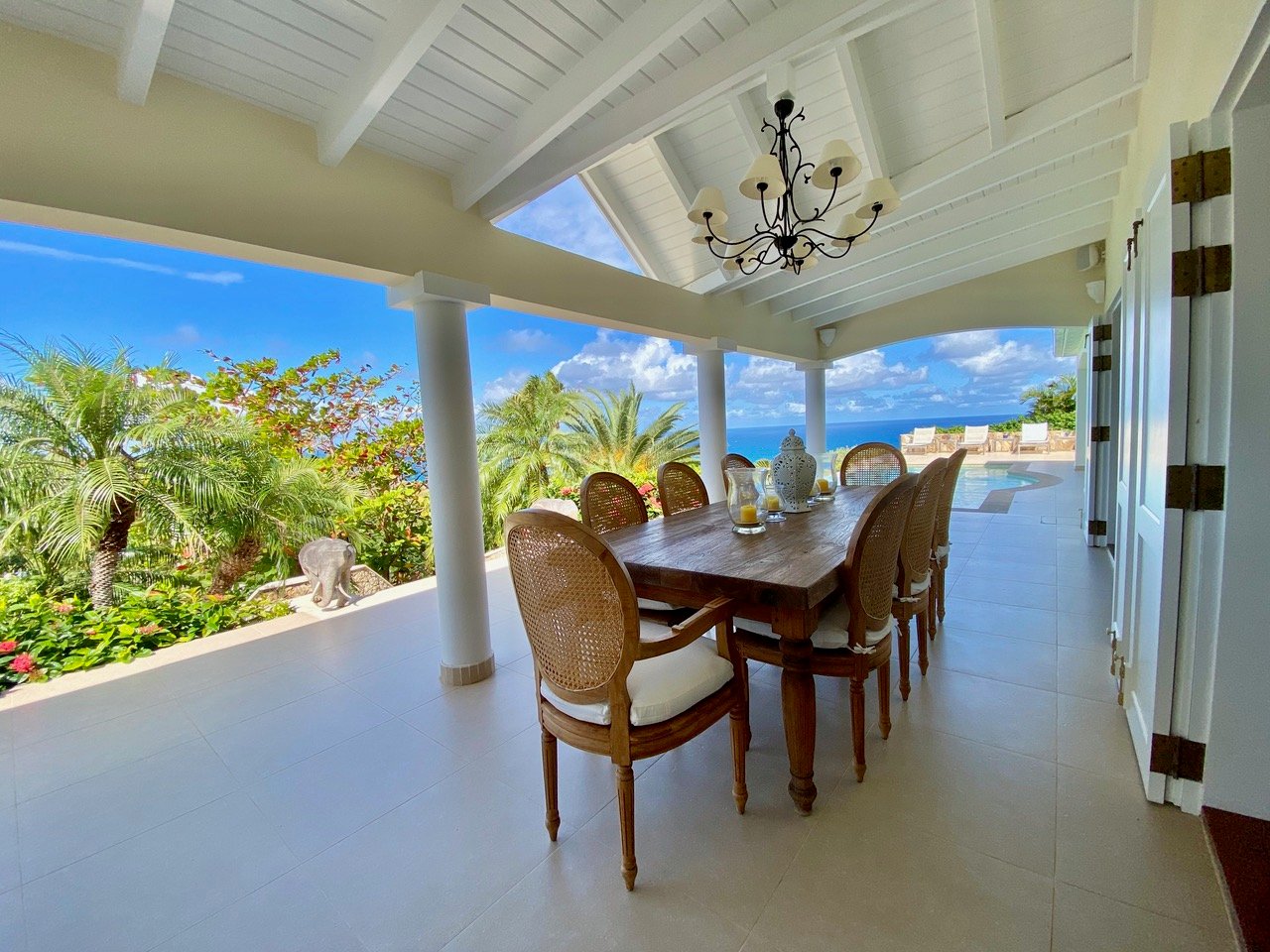 Elegant covered dining terrace with wooden table, chandelier, and ocean views at a luxury villa in St Barts