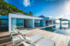 Sunlit terrace with loungers beside the infinity pool at private villa rentals St Barts overlooking lush hills.