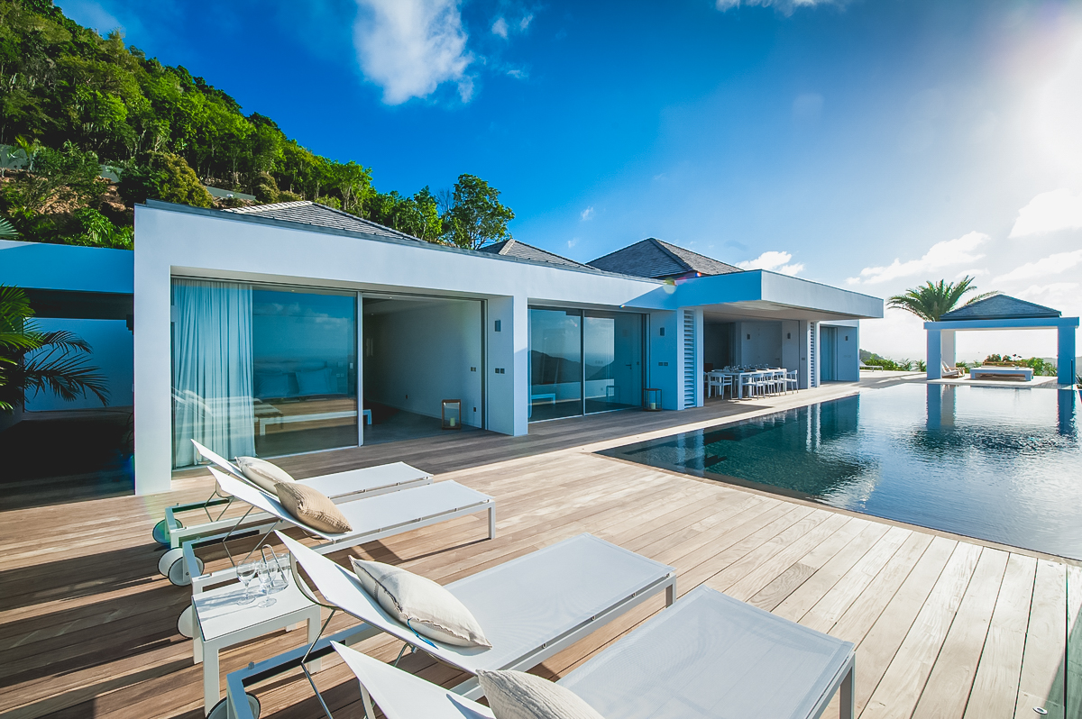 Sunlit terrace with loungers beside the infinity pool at private villa rentals St Barts overlooking lush hills.