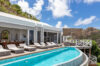Luxury st barts villa with curved infinity pool, ocean view, and sun loungers under blue sky.