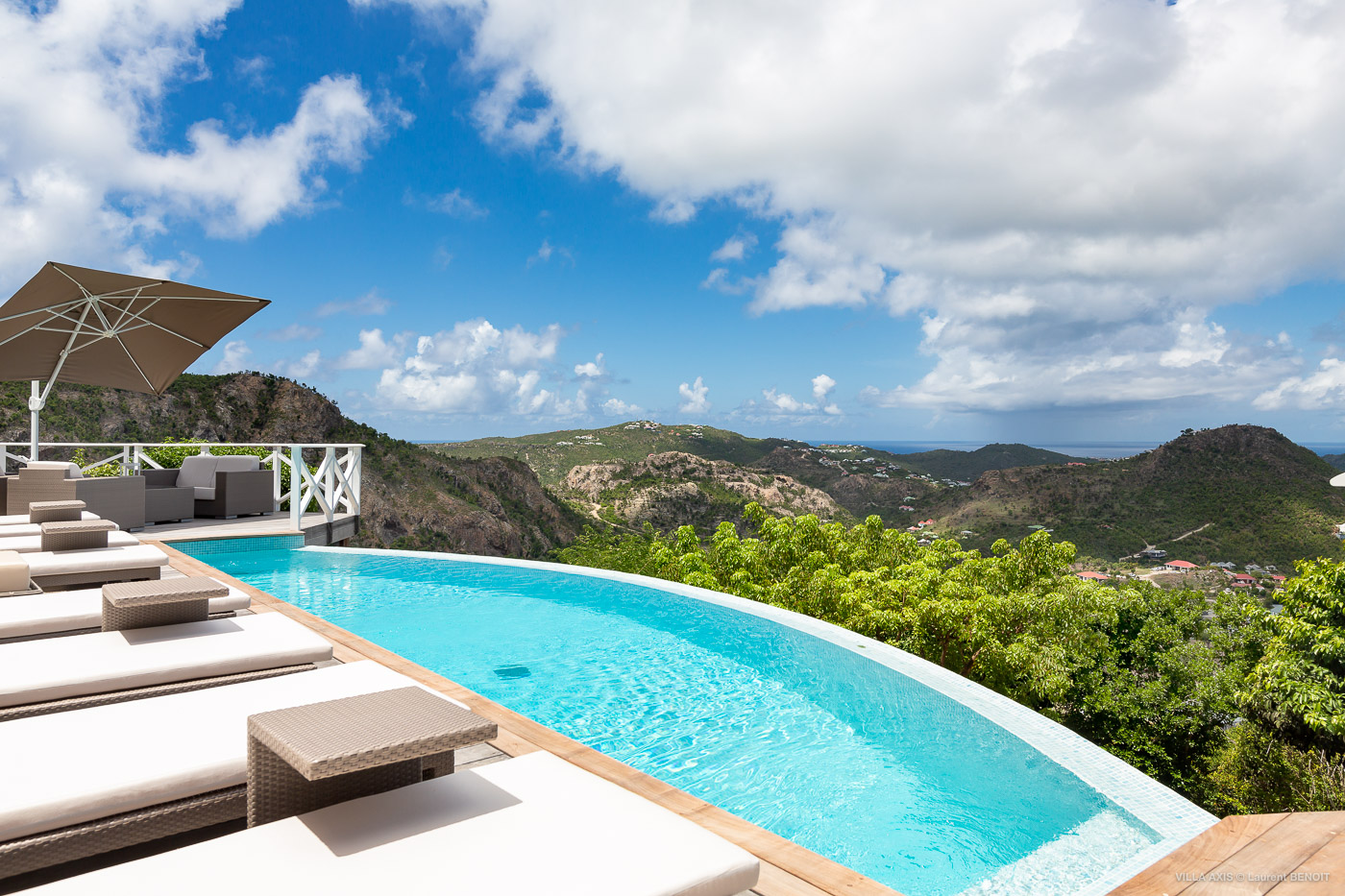 Curved infinity pool at luxury st barts villa with panoramic mountain and ocean views.