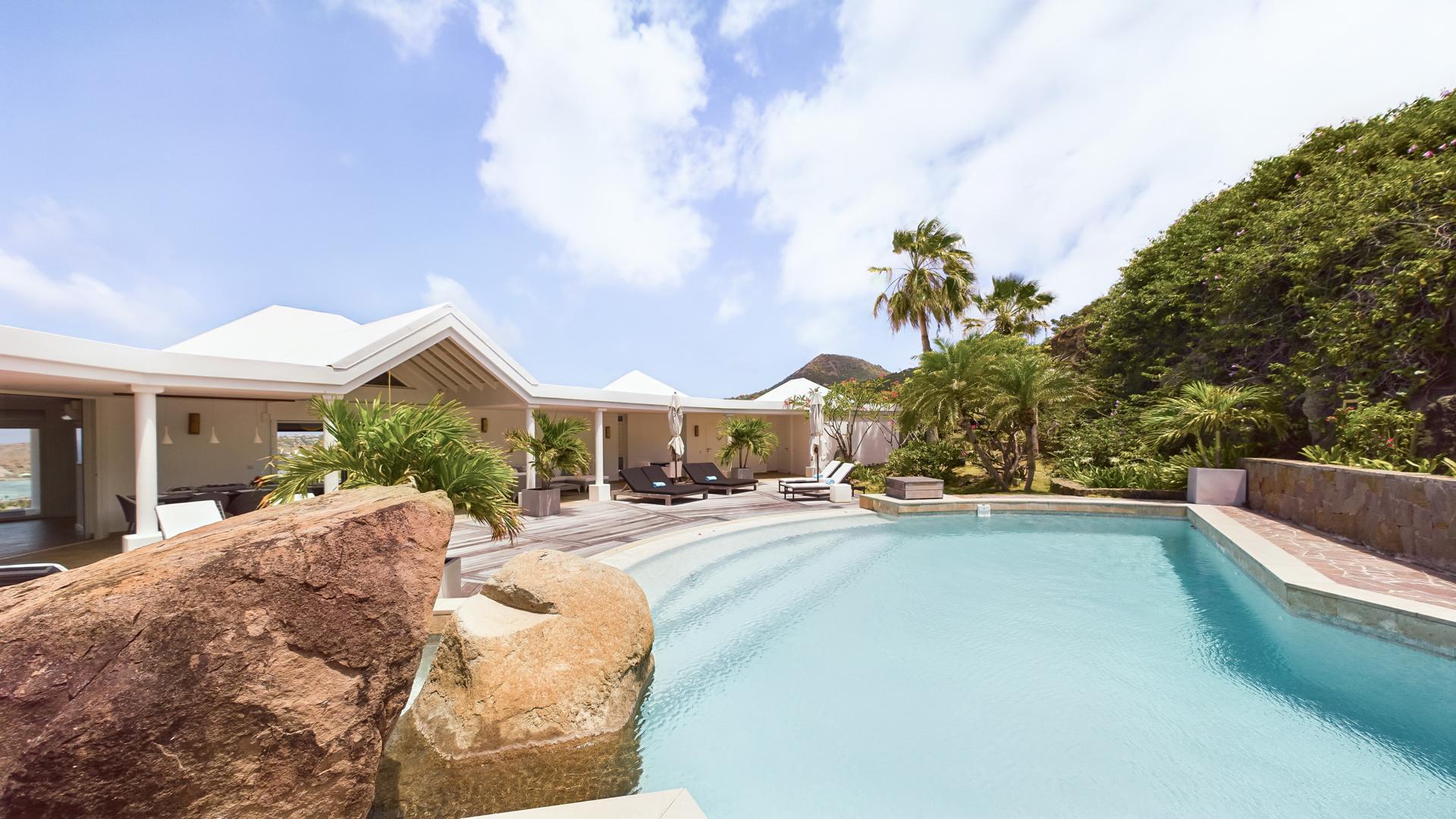 Curved infinity pool surrounded by tropical gardens at st barts villa rentals with open terrace and modern architecture.