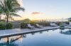 Sunset view over infinity pool at luxury st barts villa surrounded by palm trees and hills.