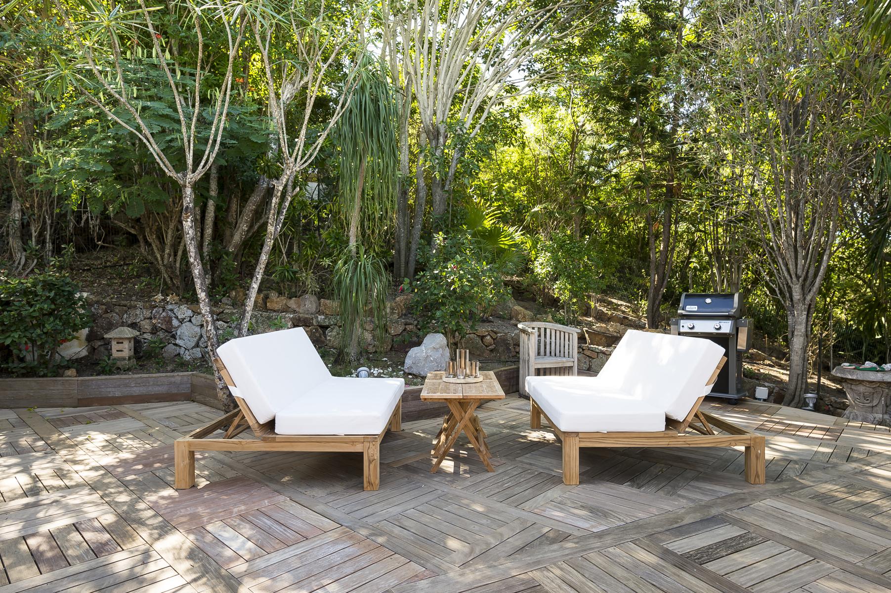 Private villa rentals in St Barts with two white sun loungers on a wooden deck surrounded by lush tropical greenery.