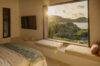 Serene bedroom with a large picture window overlooking the ocean and hills at sunset